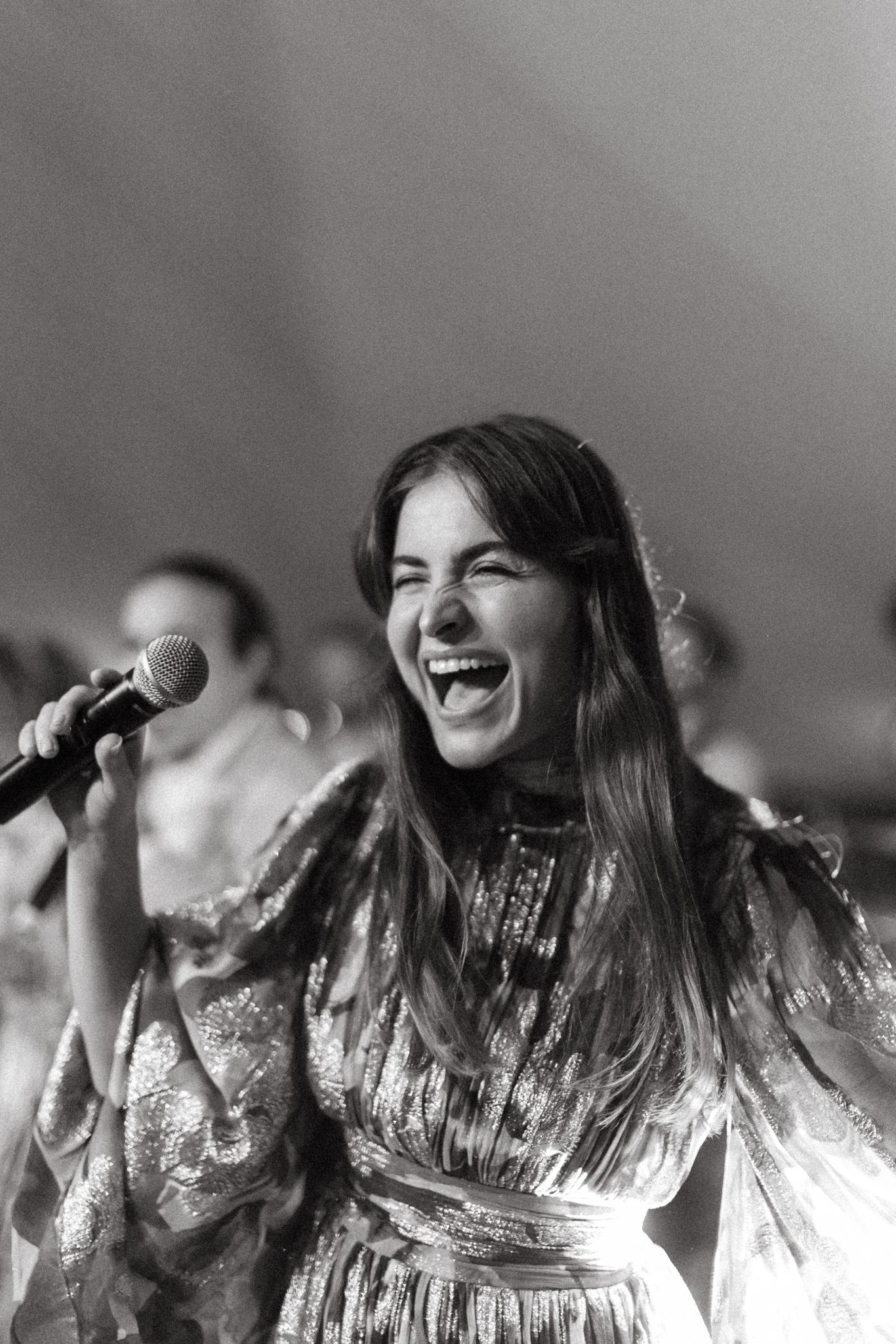 Maya smiling as she sings into a microphone