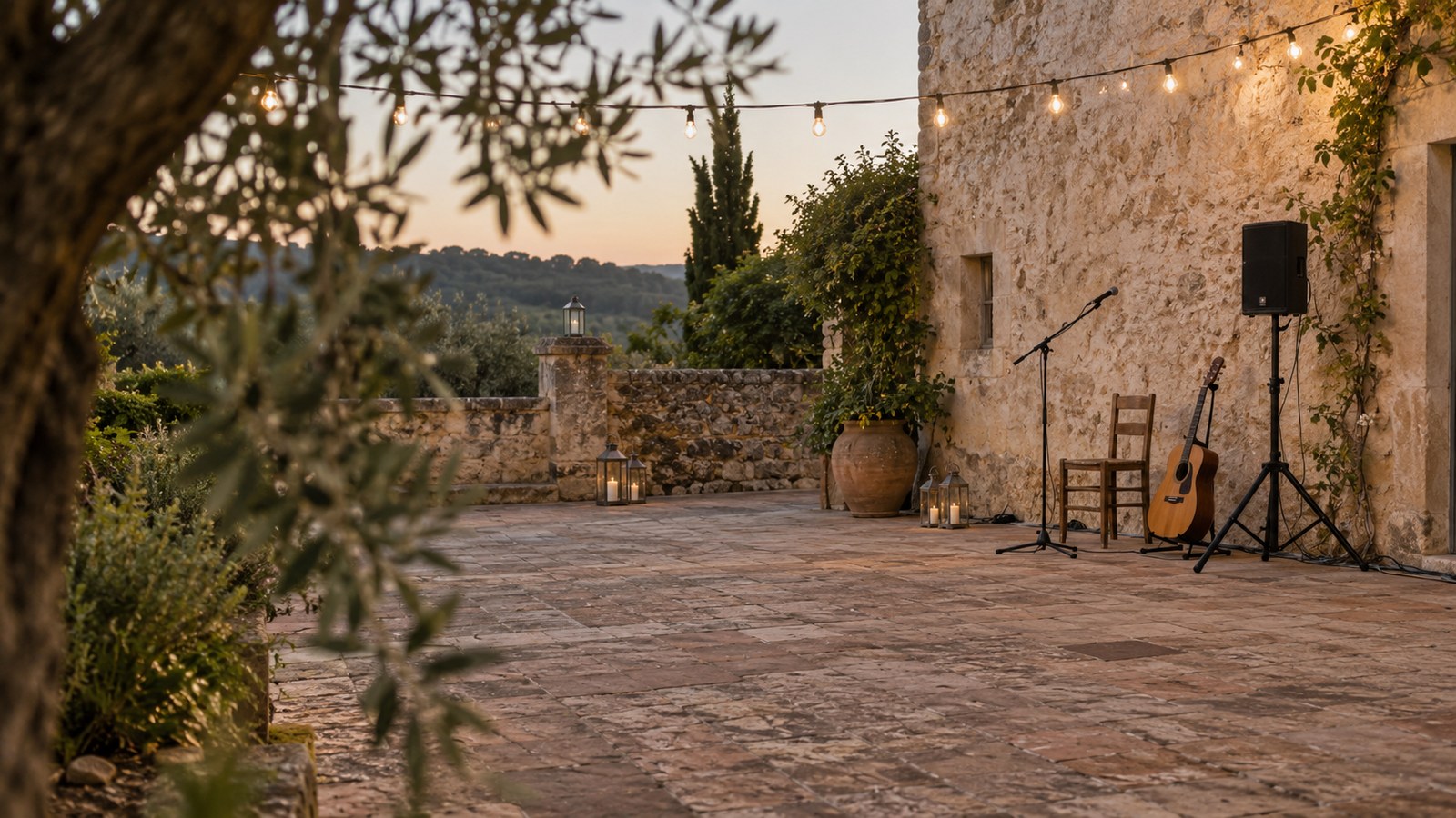 Empty limestone courtyard prepared for a first dance, with a discreet music corner in early evening light.